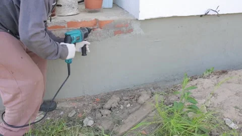 Dismantling red brick. A man chips away bricks around the foundation of a house 库存影片 250936560