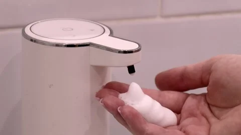 Dispensing foam soap onto bare hand from white touchless dispenser with chrome Stock Footage 314364202