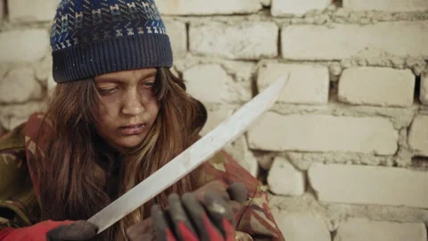 Displaced Minor Sharpens Cutlass on Stone in Harsh Shelter 스톡 동영상 347087608