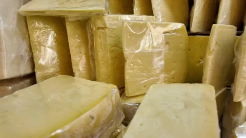 Display of assorted cheese wedges and blocks in plastic wrap at market. Stock Footage 331914553