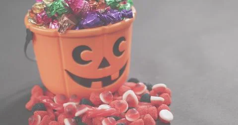 Displaying jack-o'-lantern bucket spilling foil candies and gummy sweets on dark Photos