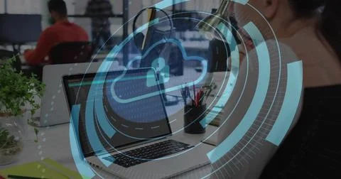 Displaying laptop with cloud lock overlay at open-plan office desk, coworker Stock Photos