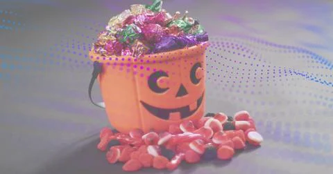 Displaying orange jack-o-lantern bucket holding foil-wrapped sweets on gray t Stock Photos