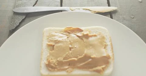 Displaying white bread topped with peanut butter on rustic wooden table, with Stock Photos
