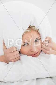 Displeased woman covering ears with pillow in bed Stock Photos