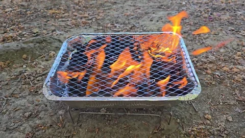 Disposable barbecue grill with burning flames and hot charcoal on the ground Stock Footage 341676810