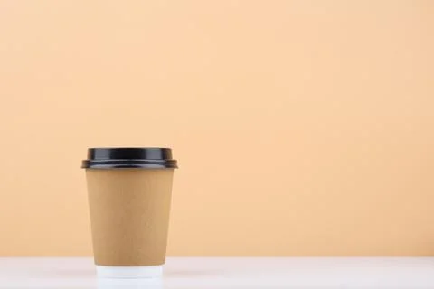 Disposable coffee cup on white table against light beige background with copy Stock Photos