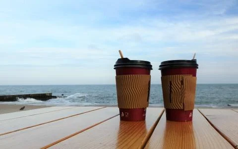 Disposable cups of coffee standing on a table against the blue sea. Coffee cu Stock Photos