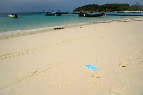 A disposable facemask thrown on the beach Stock Photos