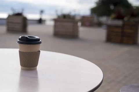 Disposable paper cup on a cafe table against a bright blue sky. Concept of Stock Photos