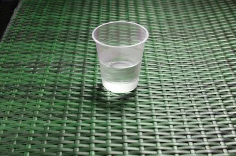 Disposable plastic cup half filled with water on the green table Stock Photos