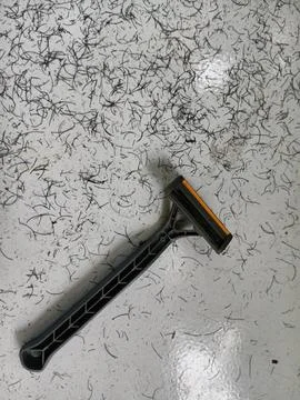 Disposable plastic razor on white tiled floor covered in cut hair Stockfoto's