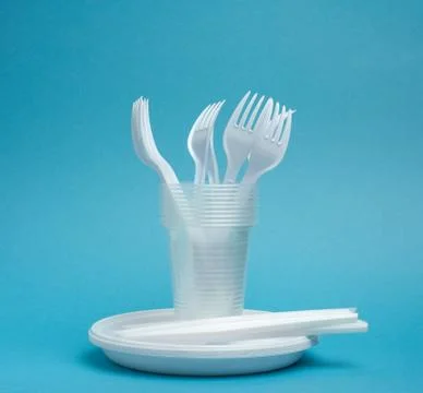 Disposable plastic tableware plates, cups, forks and knives on a blue backgro Stock Photos