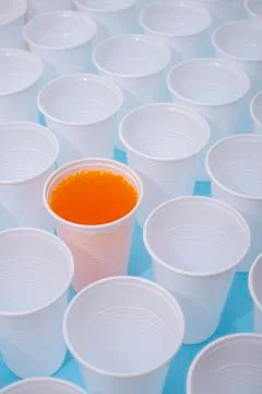 Disposable plastic white empty cups and one glass filled with orange lemonade Stock Photos