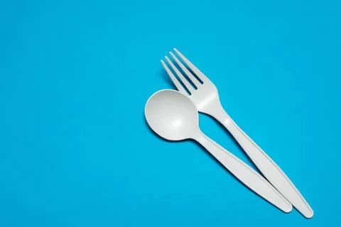 Disposable spoon and fork made of corn starch on a blue background. Stock Photos