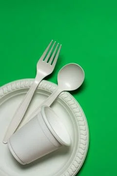 Disposable spoon, fork, glass and plate of corn starch on a green background. Stock Photos