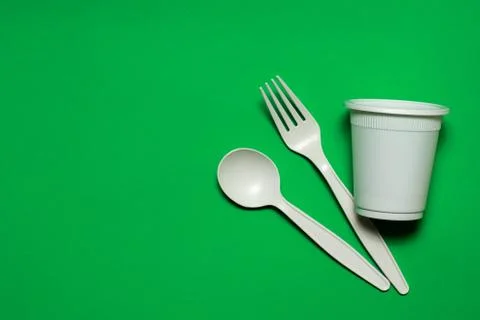 Disposable spoon, fork, glass of corn starch on a green background. Stock Photos