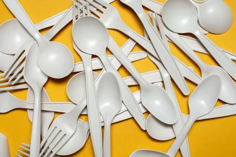 Disposable spoons and forks of corn starch lie on a yellow background. Фото