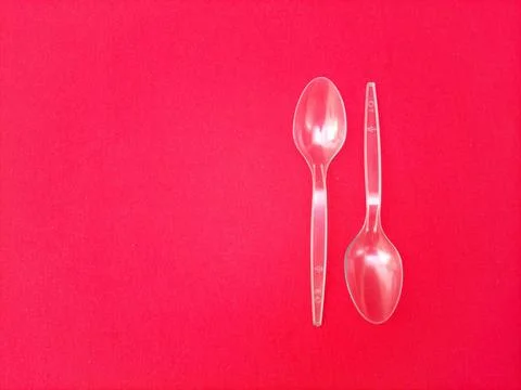 Disposable transparent plastic spoons aligned on red background with copy space Stock Photos