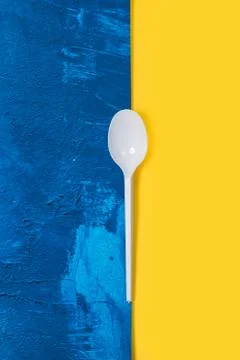 Disposable white plastic spoon on a classic blue and yellow background Foto stock