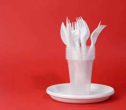 Disposable white plastic tableware plates, cups, forks and knives on a red ba Stock Photos