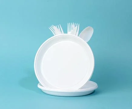 Disposable white plastic tableware plates, cups, forks and knives on a blue b Stock Photos
