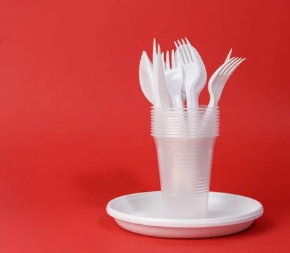 Disposable white plastic tableware plates, cups, forks and knives on a red... Stock Photos