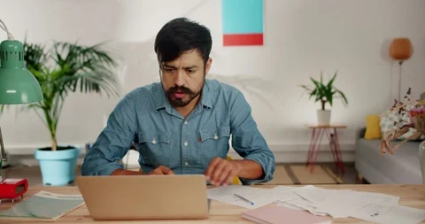Dissatisfied Hispanic young man getting angry during work using computer at Stock Footage 120745005
