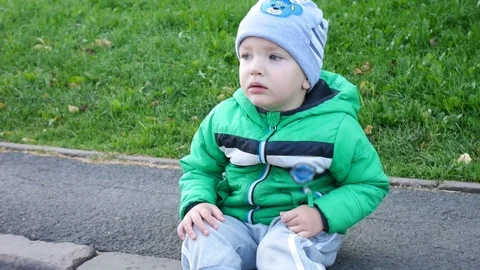 Dissatisfied Litte Boy Wearing a Jacket Sitting on the Curb Stock Footage 122486115