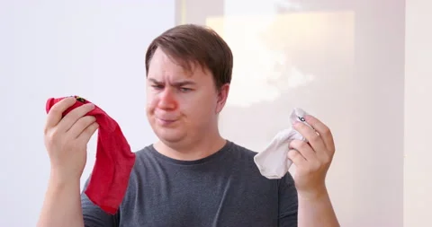 Dissatisfied man looks at different socks taking red to wear Stock Footage 217615628
