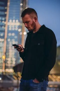 Dissatisfied man using smartphone texting. Male standing in the city in the Stock Photos