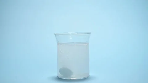 Dissolution of effervescent tablet in glass with water over blue background Vidéo 238072002