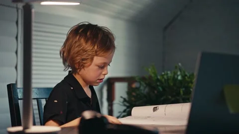 Distance learning, a boy sits at a table at home looking in a beech laptop. The Vídeos de archivo 166603820