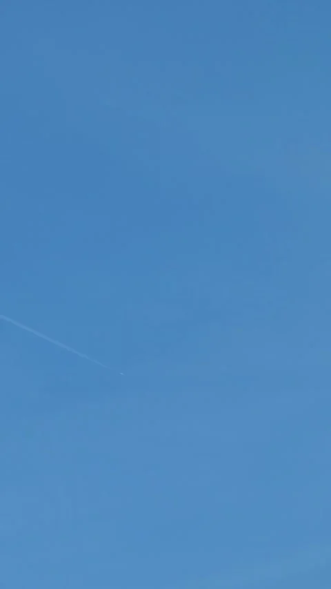 Distant airplane flying high in a clear blue sky leaving a white vapor trail Stock Footage 332998625