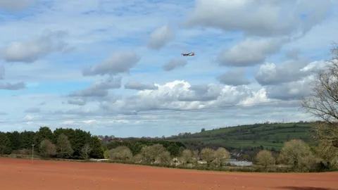 Distant airplane flying over ploughed field panning Stock Footage 331584513