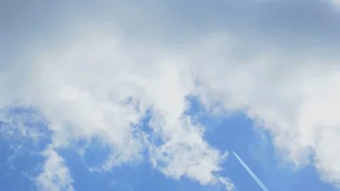A distant airplane passes high overhead, leaving a jet contrail against a cloudy Stock Footage 74675325