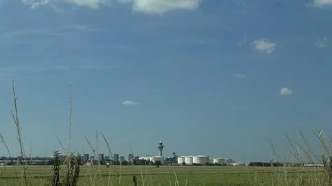 Distant airport control tower and industrial tanks above wide green field Stock Photos
