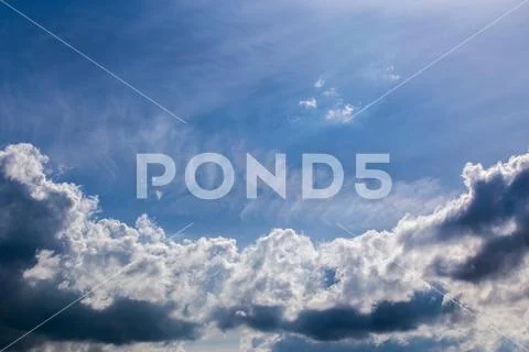 Distant backlit cumulus and feather clouds near horizon closeup telephoto shot Stock Photos