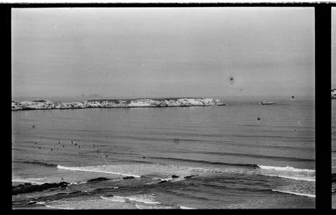 Distant Bathers Beneath an Offshore Rock Formation Stock Photos