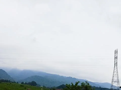 Distant blue mountains under a cloudy sky with a tall metal tower Stock Photos