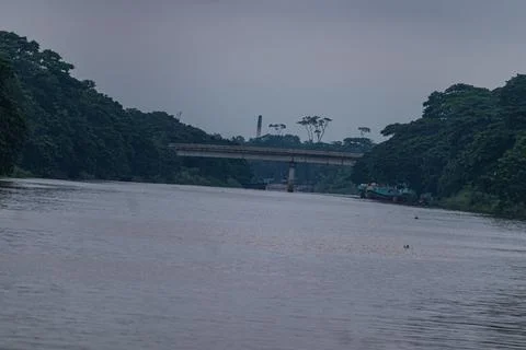 Distant bridge view with river and boats during overcast weather in rural ar Stock Photos