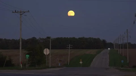 A distant car drives down a lonely country road at night with a full moon Stock Footage 164450175