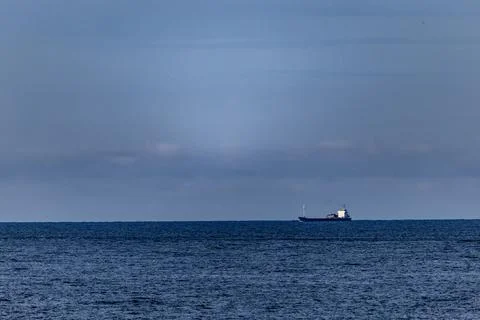 Distant Cargo Ship Against Expansive Ocean and Tranquil Sky Stock Photos