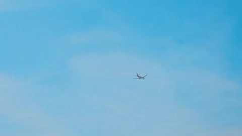 A distant commercial airplane soars through a bright, clear 스톡 동영상 321700838