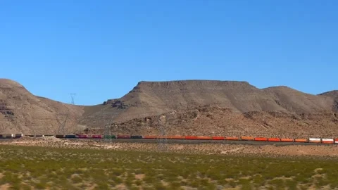 Distant commercial train swiftly crosses arid valley beneath clear blue sky Stock Footage 304734349