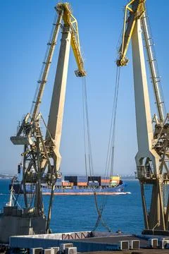 Distant container ship between two floating port cranes on a sunny day Stock Photos
