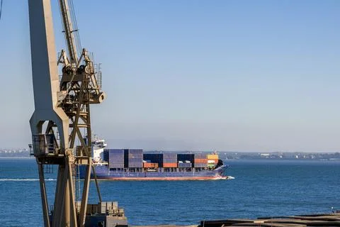 Distant container ship passing harbour and cranes fully loaded in sunny day Stock Photos