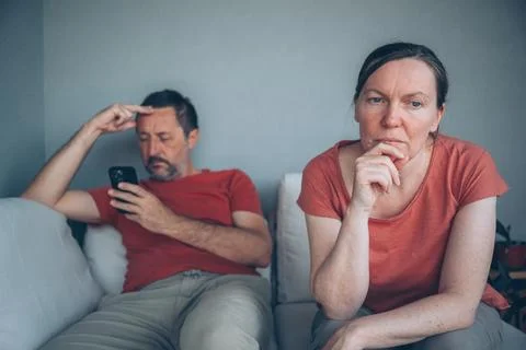 Distant couple sitting on sofa during relationship strain while man focuses.. Stock Photos