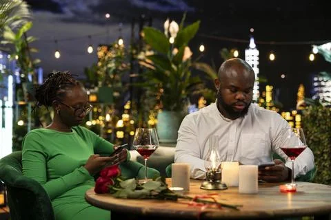 Distant couple uses smartphone during rooftop restaurant date instead of talking Fotos Stock