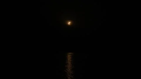 Distant crescent moon glowing over calm dark sea with narrow golden reflection Stock Footage 346028517